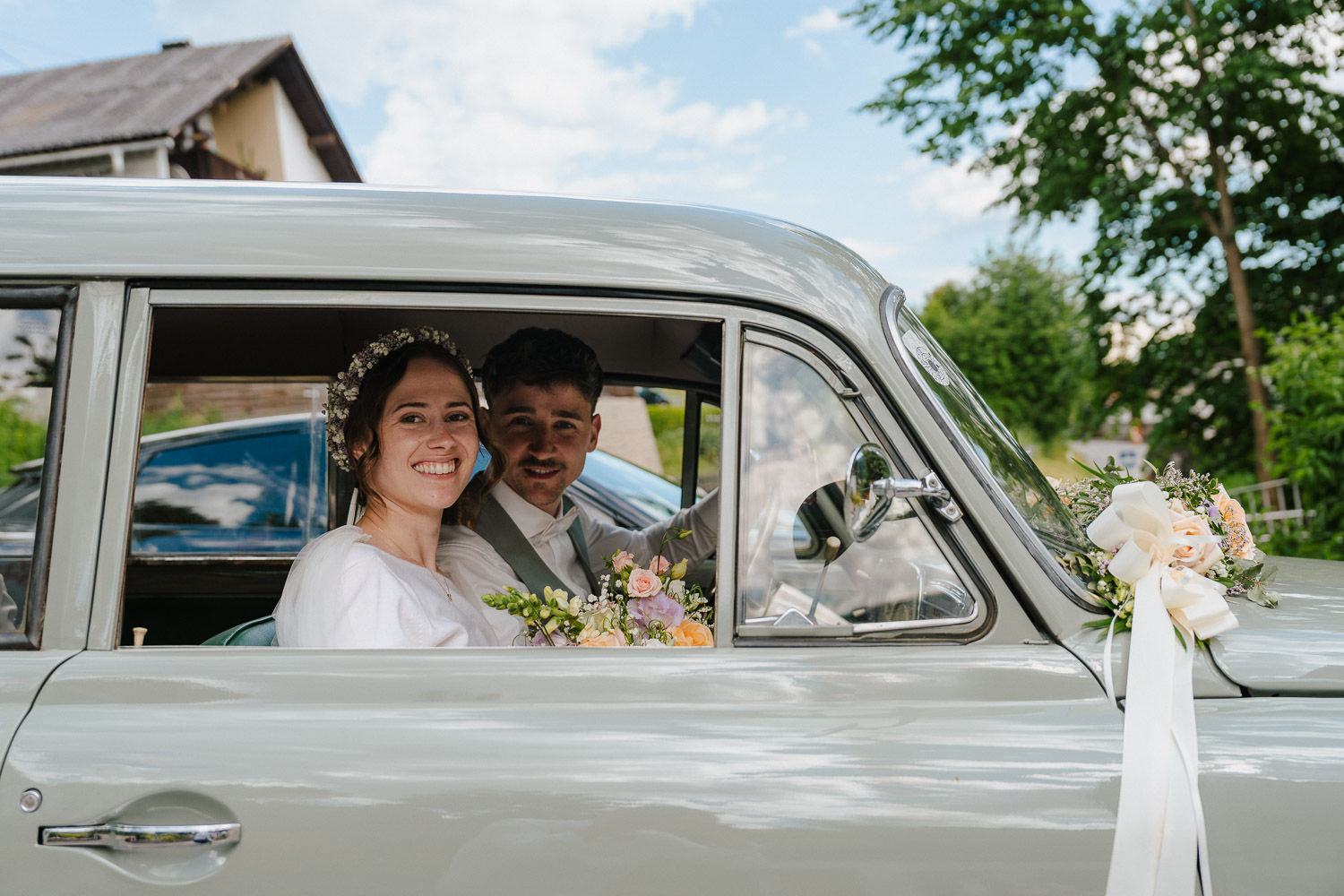 Dier Braut blickt aus dem Fenster des Hochzeitsautos mit dem Bräutigam im Hintergrund
